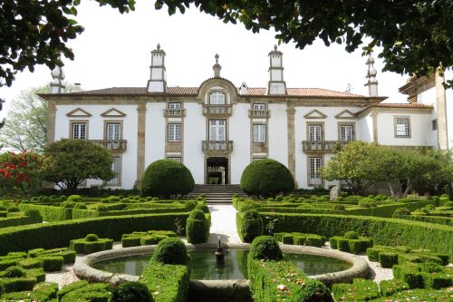 A white palace with a small moat and green hedges in front 