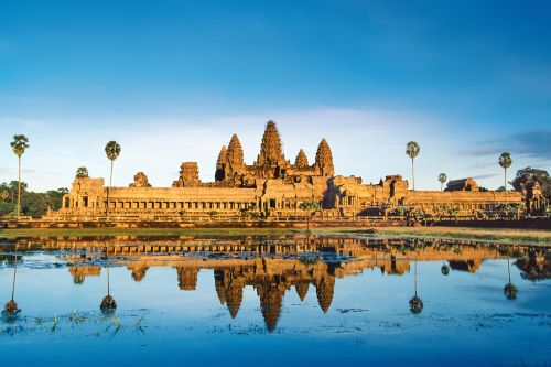 The majestic Angkor Wat temple complex against a bright blue sky reflecting in the water