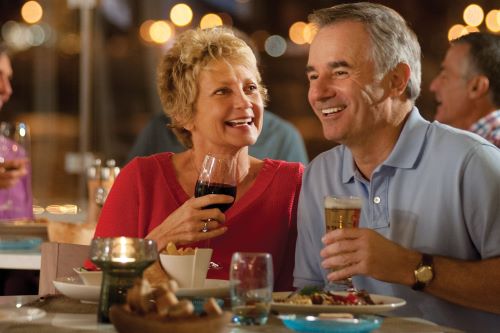 A couple enjoying a dinner and drinks at night with lights glittering behind them