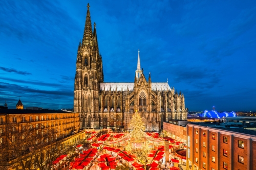 A Christmas market lighting up with a Christmas tree in the middle and the majestic church in the background