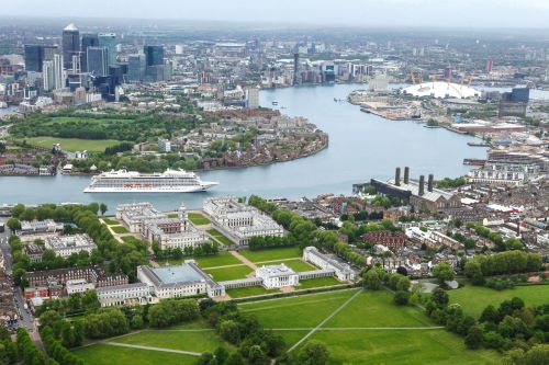 A cruise ship cruising through Greenwich in London surrounded by buildings and green gardens and landscape 