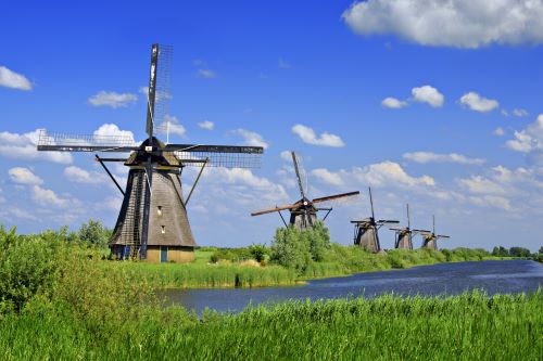 A handful of traditional Dutch windmills standing in a row on a green filed