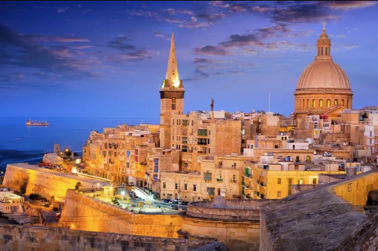 View of Valletta with its honey-coloured limestone building set against the Mediterranean Sea at dusk. 