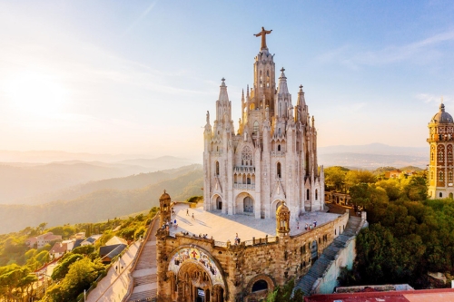 A large, ornate church on a hill with a tall central tower topped by a statue of Christ, surrounded by picturesque countryside.