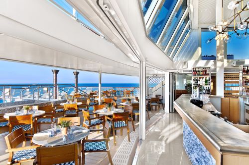 A restaurant onboard a cruise ship with light interiors and table and chairs