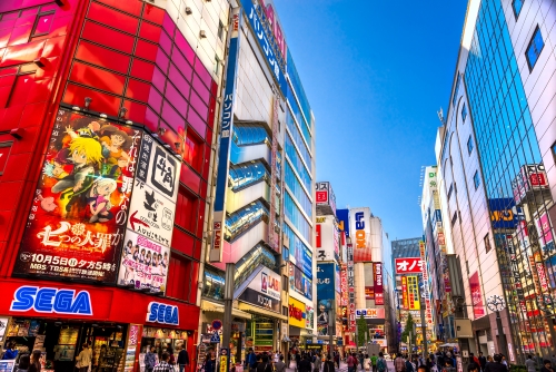 A vibrant, neon-lit street filled with towering arcade centres and flashing screens in the Akihabara's gaming district in Tokyo. 