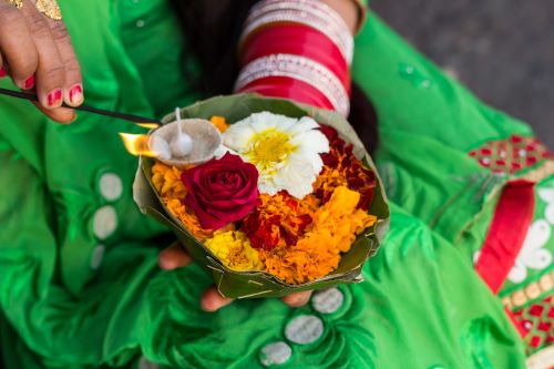 Closeup photo of an offerings plate held by a woman's hand including nicely arranged flowers and a candle which is being lit by her other hand. 