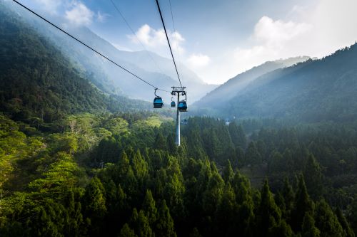 A cable car above lush forest landscape surrounded by mountains and low hanging clouds