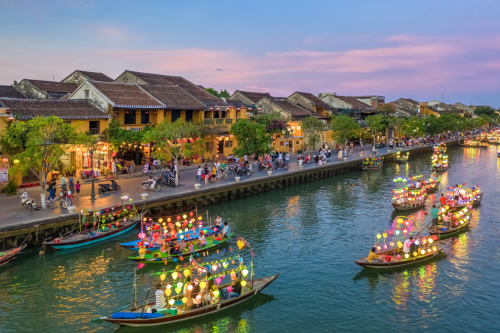 Colourfully lit up boats cruising down the river in Hoi An at dusk 