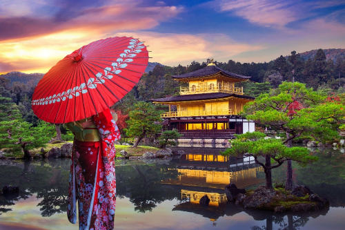 A woman wearing a kimono and holding a parasol is looking out to a beautiful Japanese temple surrounded by a lake