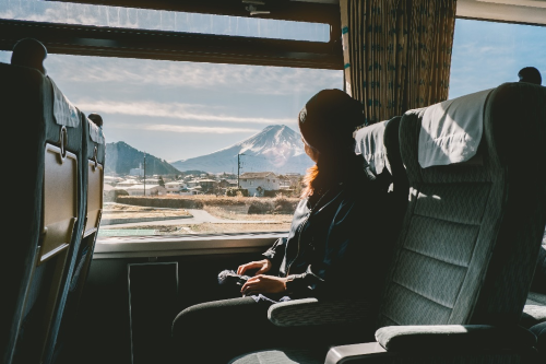 A traveller sitting in a train with large windows and looking out on Mt Fuji 
