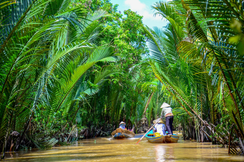 Two small boats cruising down the Mekong Delta along lush greenery 