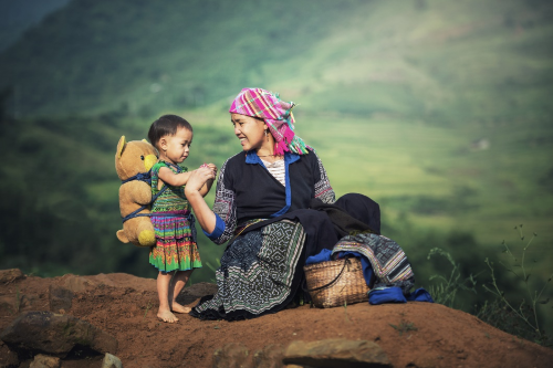 A beautiful woman attending to a small child, both wearing traditional dresses. 