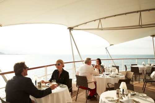 Couples enjoying lunch on deck in the sunshine overlooking the sea