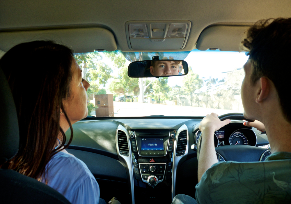 Learner driver and supervisor in car looking in rear view mirror