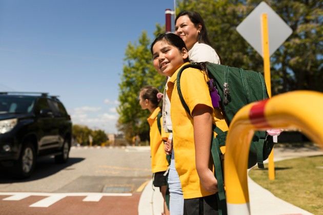 Two school children and their parent looking in both directions before crossing the road