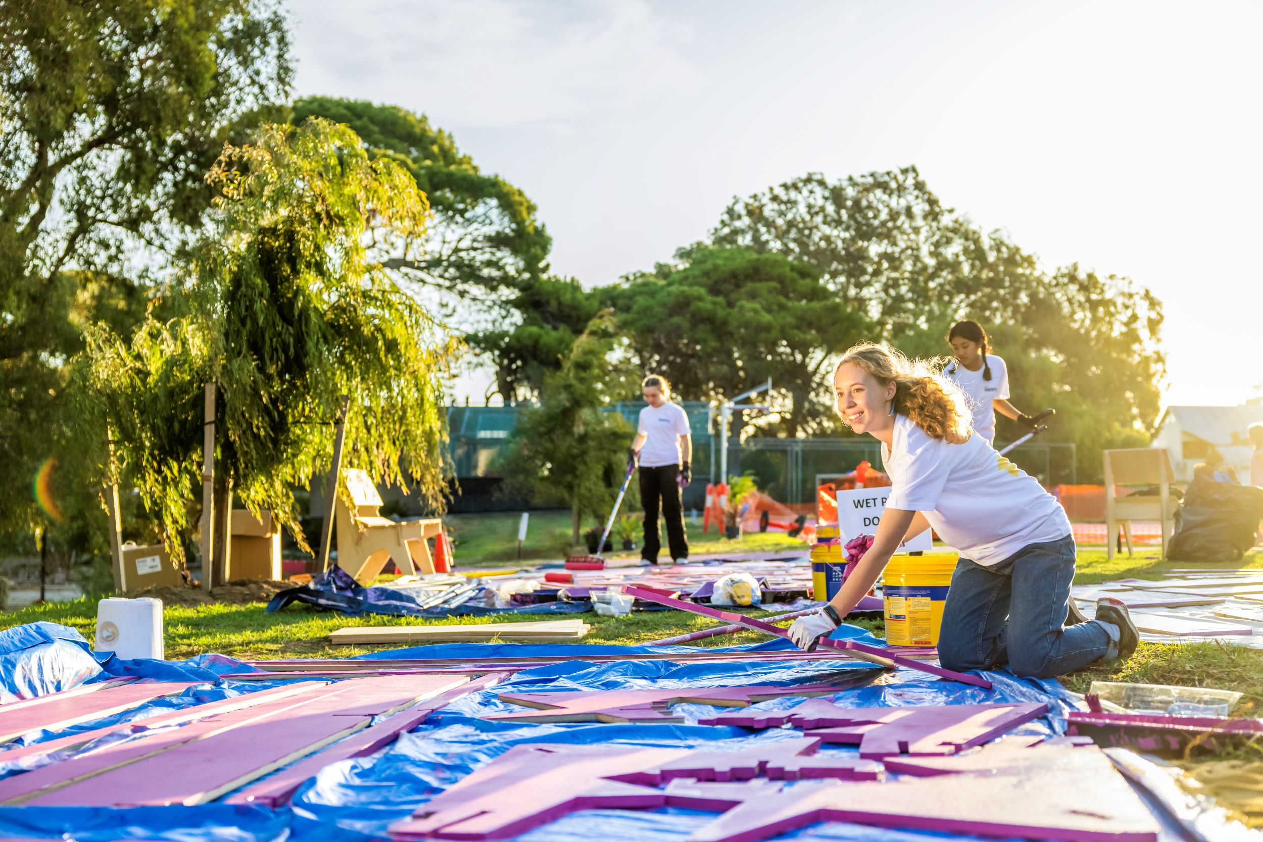 Young people paint outdoor furniture bright purple in a sunny local park