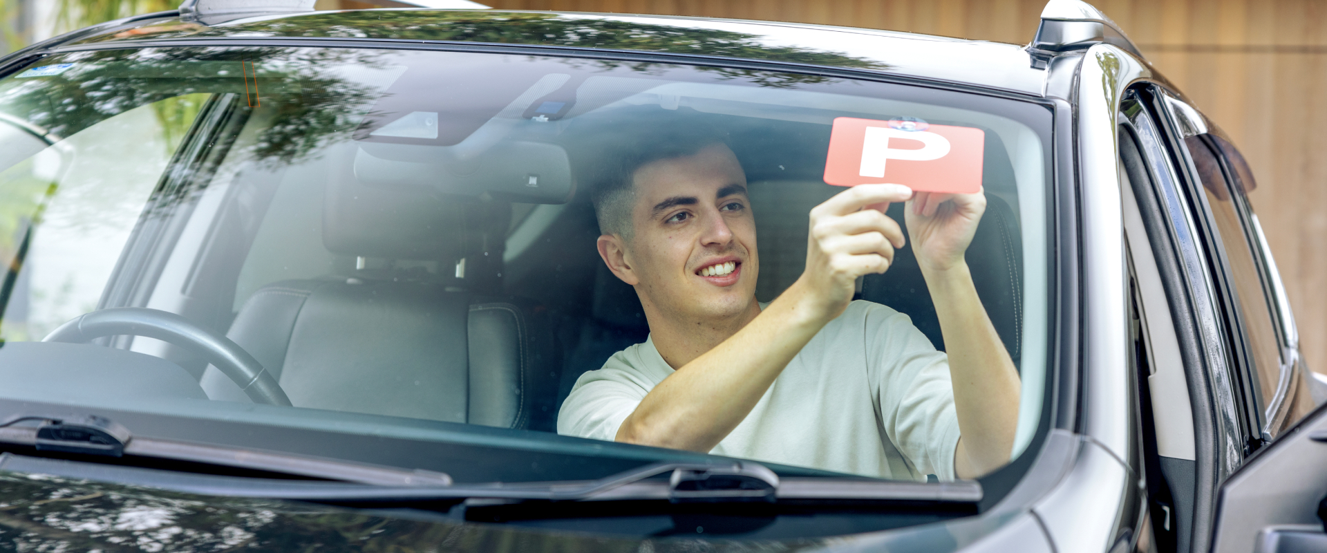 Young male putting red P Plate on front window of car