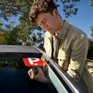 A male teen attaches a red P plate to the interior of a car's windshield